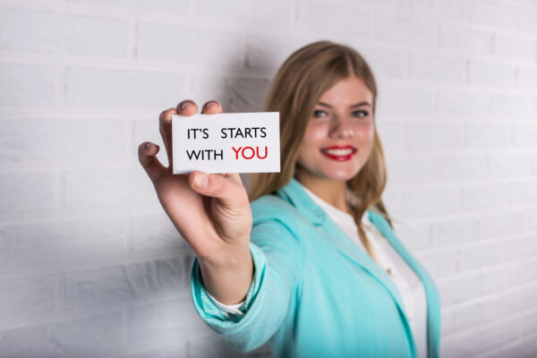 Motivational business quote. Business person in suit hold card with message. It Starts With You!